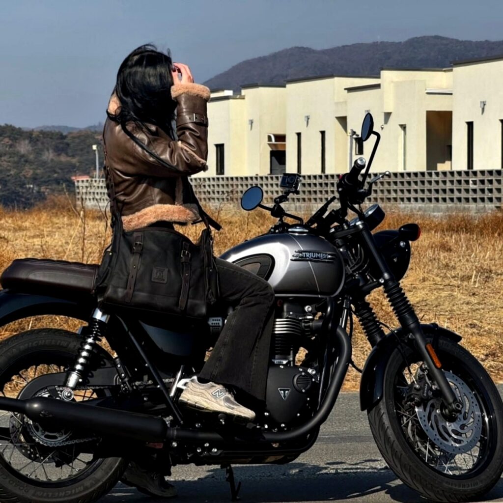 A woman on a Triumph motorcycle wearing a dark oak Builford Classic Hobo messenger bag.