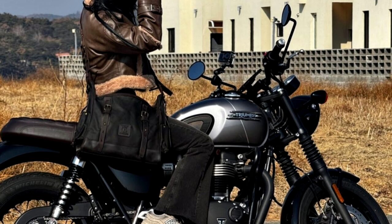A woman on a Triumph motorcycle wearing a dark oak Builford Classic Hobo messenger bag.