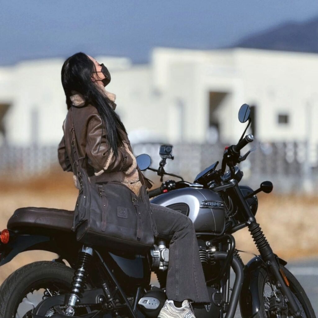 A rider looking up while seated on a motorcycle, highlighting the secure fit of the Builford messenger bag.