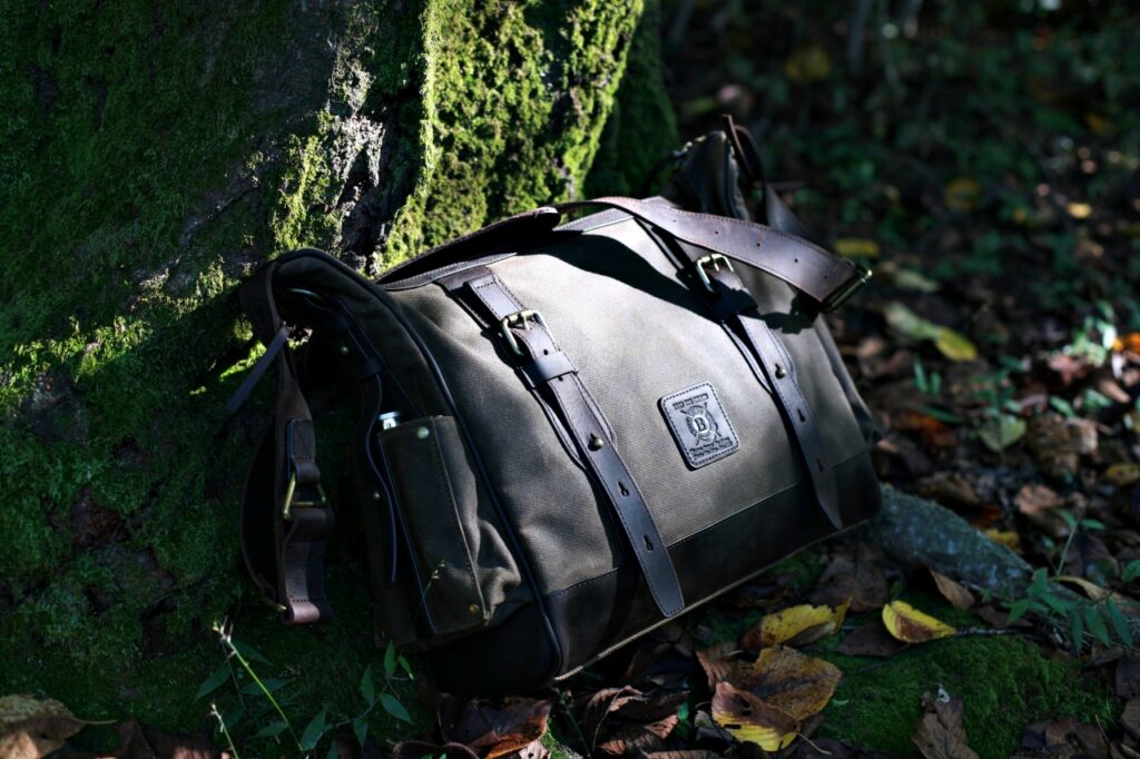Close-up of a Builford messenger bag leaning against a mossy tree, showing the rich texture of waxed canvas.